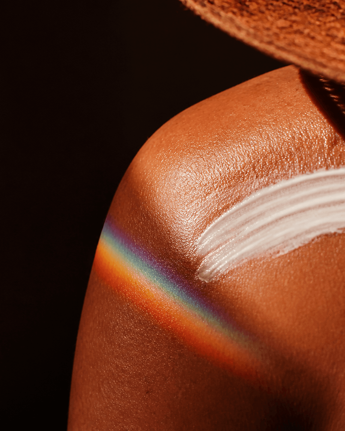 Close-up editorial photograph of real skin with a swipe of sunscreen under sun and prism light.
